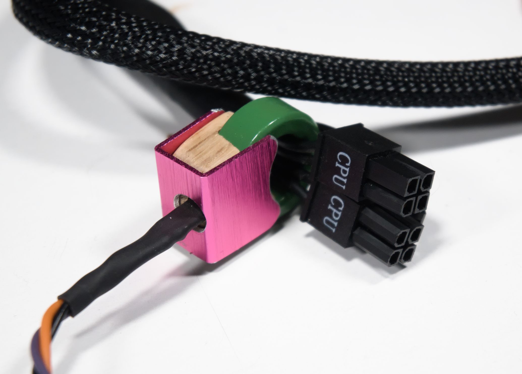 A CPU power cable, with the 12V wires passing through the green toroidal core. The sensor is inserted into the gap in the core, with the wooden and aluminium mounting hardware holding it in place.