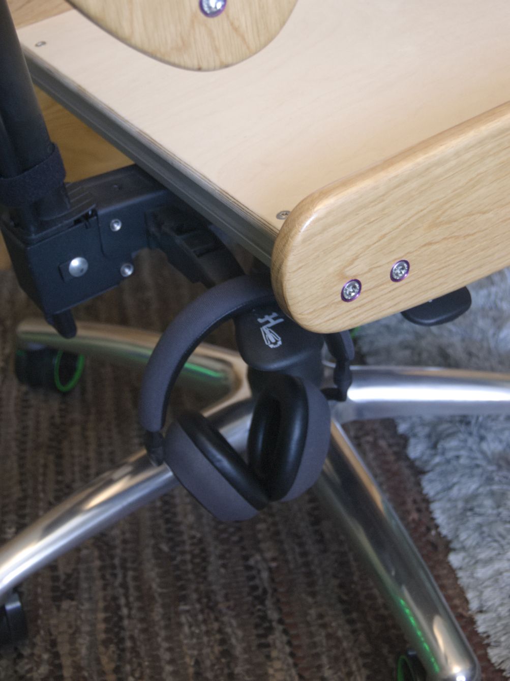 Closeup of the chair mechanism. Two levers protrude from the side, used to control the height, and the back tilting. One of the levers has a pair of headphones dangling from it.