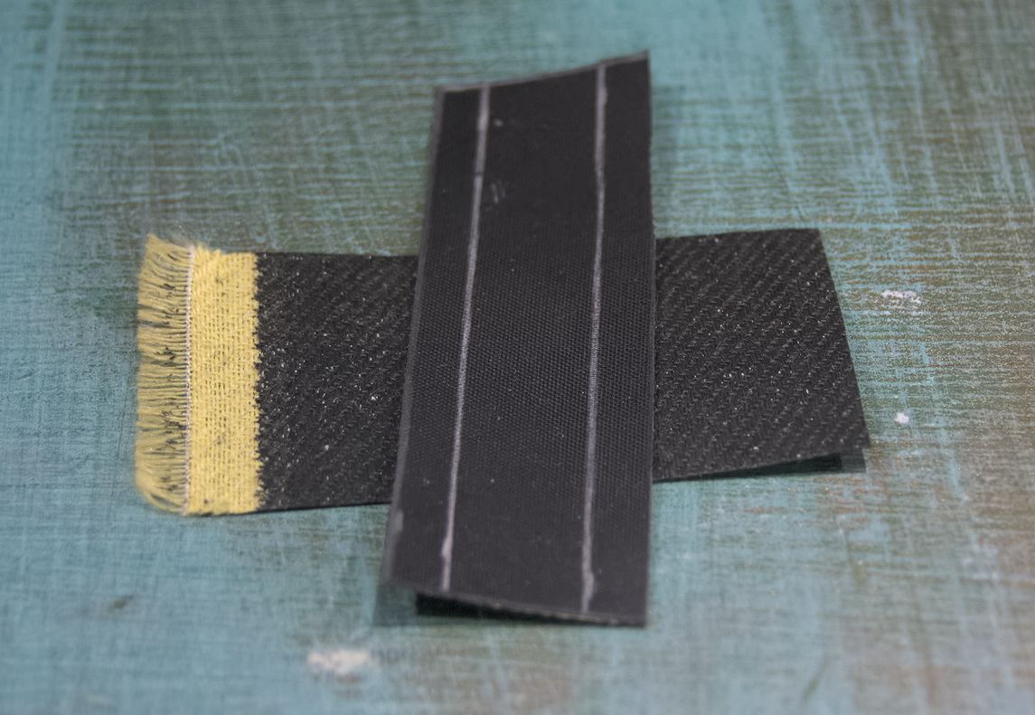 Some small pieces of Kevlar fabric coated in a black rubbery material on one side.